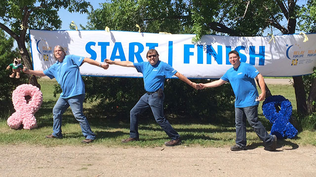 Convergint day Regina male colleagues holding hands during group photo