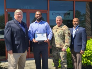 four men in front of building with one holding an award certificate