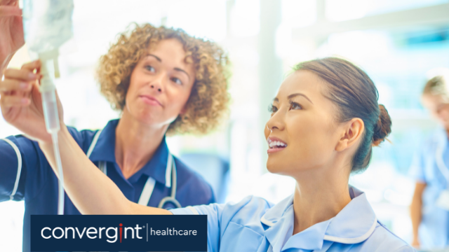 a senior nurse supervising a young nurse as she attends to a saline drip on a hospital ward