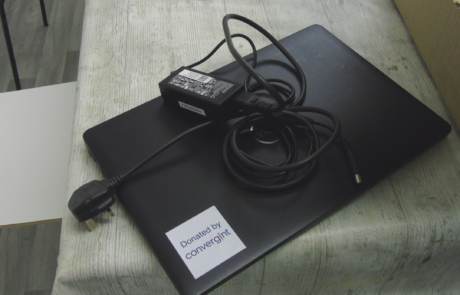 laptop on desk beside charger with a sticker saying donated by convergint