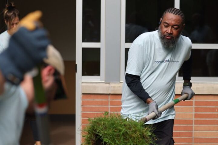 Man shoveling grass while others landscape around him.
