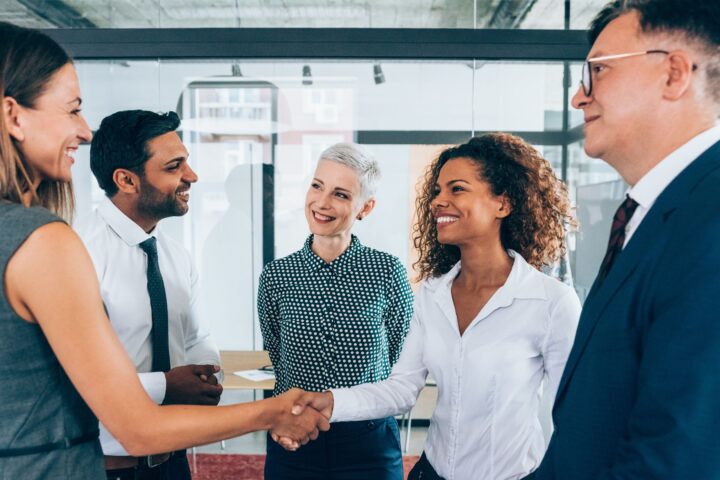 Two women shaking hands with a few other people surrounding them